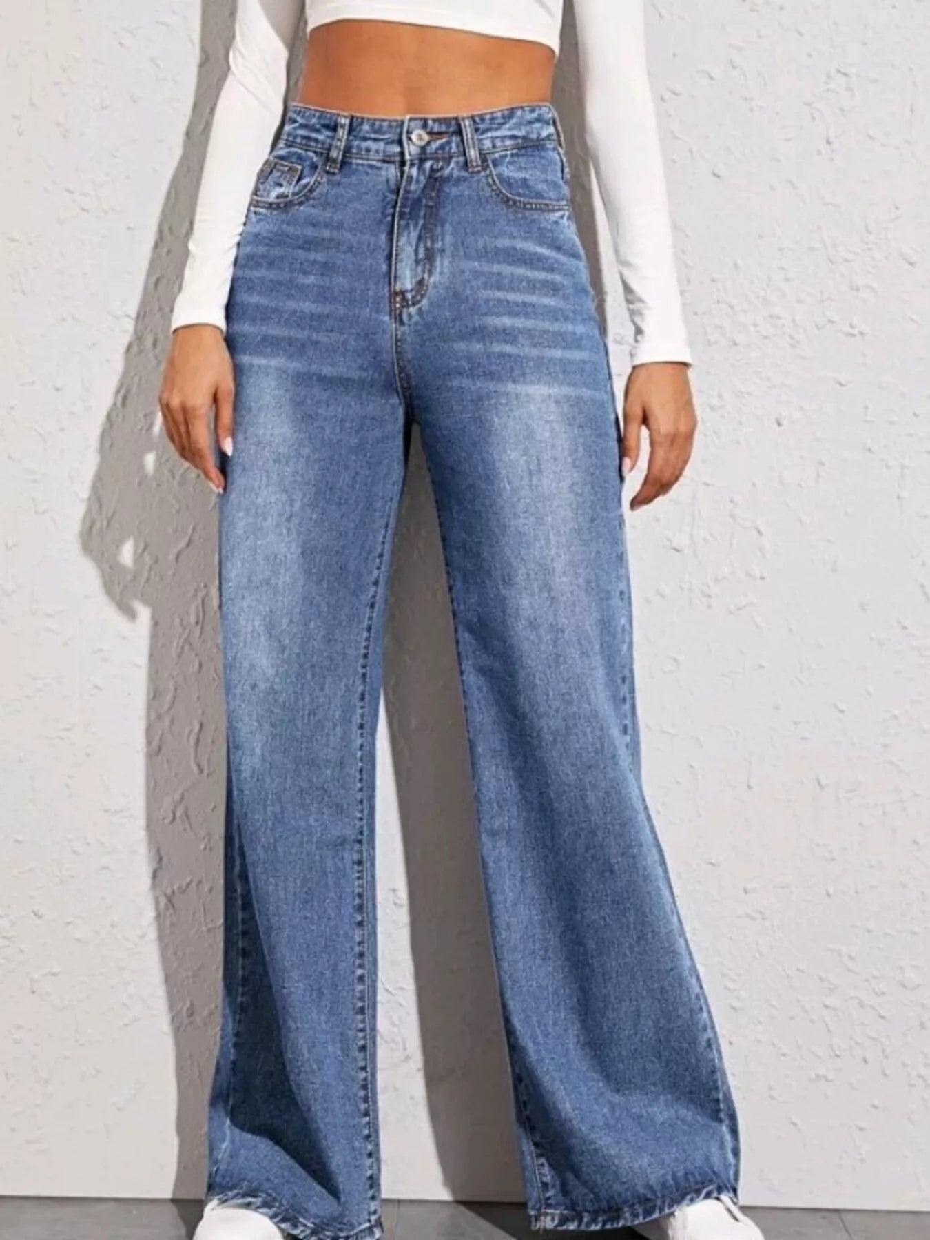 Person wearing blue wide-leg jeans against a white brick wall.