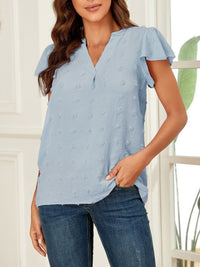 Woman wearing a light blue blouse with ruffled sleeves and dark jeans indoors.