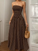 Woman wearing a brown strapless dress with white polka dots, holding a woven bag indoors.