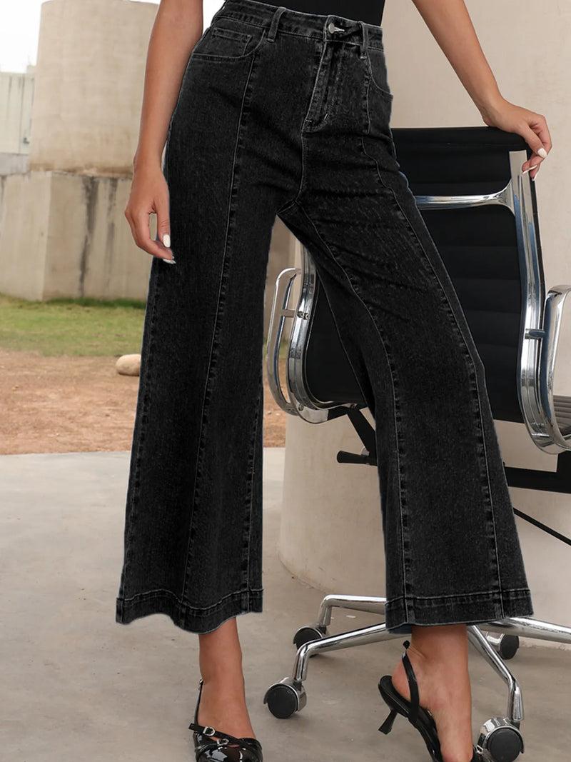 Person wearing black wide-leg jeans standing next to a chair outdoors.
