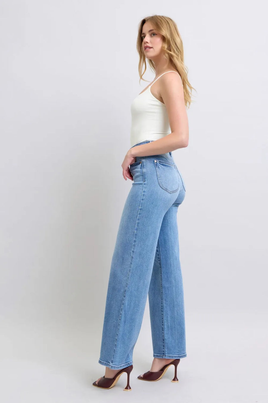Woman wearing light blue jeans and a white top on a plain background