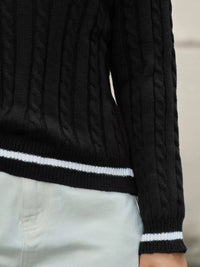 Black cable knit sweater with white trim on a neutral background