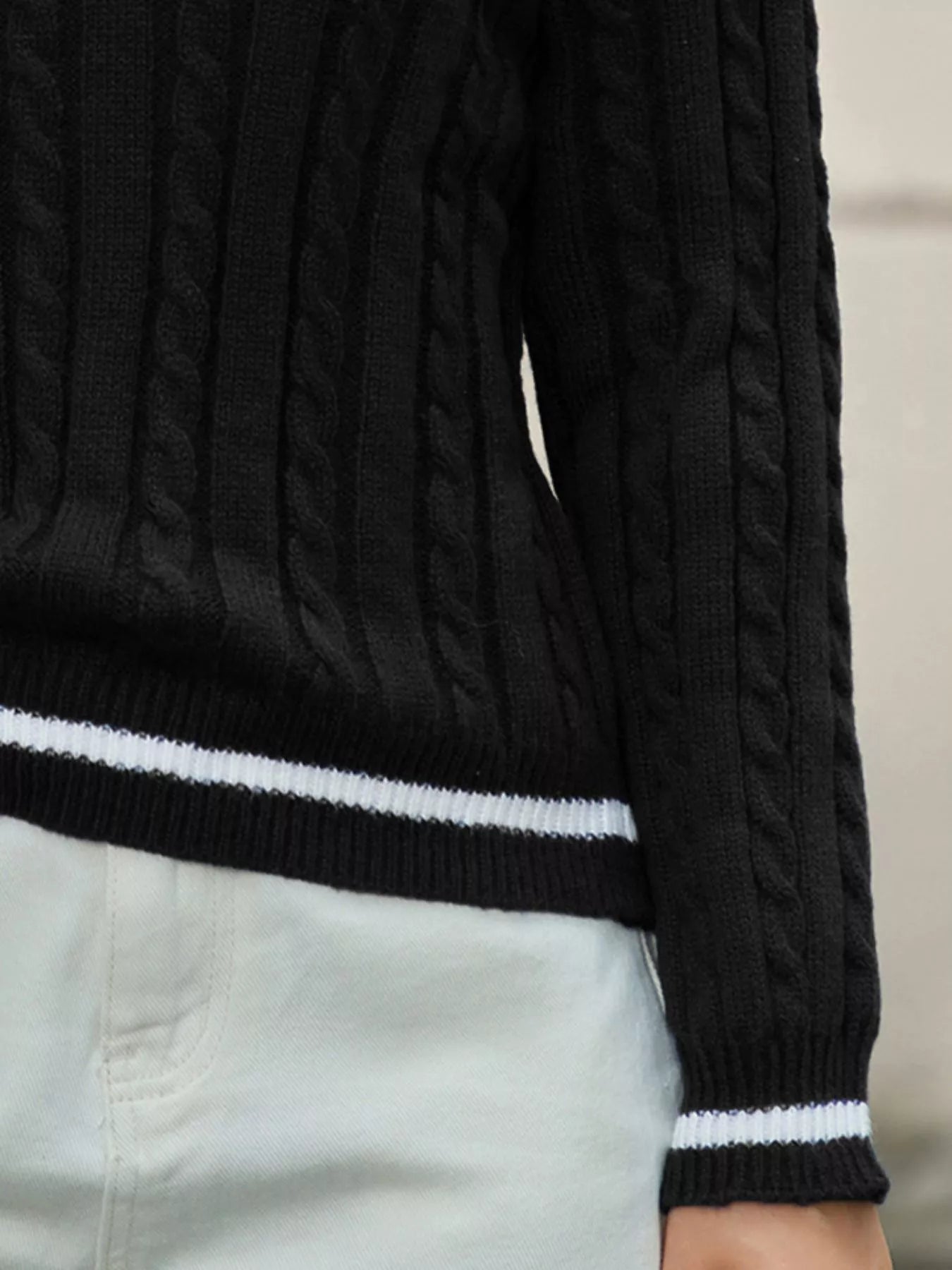 Black cable knit sweater with white trim on a neutral background