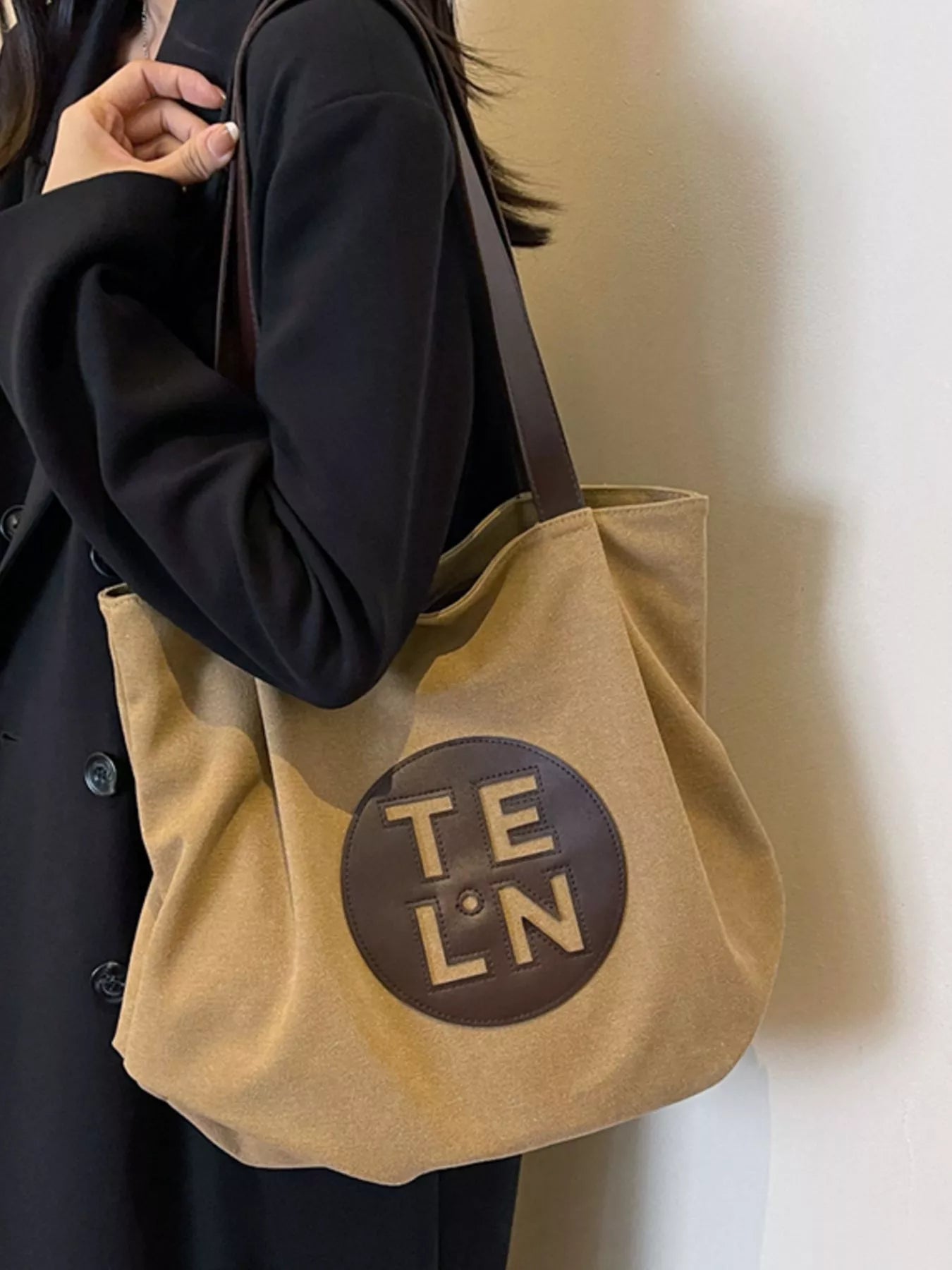 Beige tote bag with 'Teln' logo held by a person wearing a dark coat.