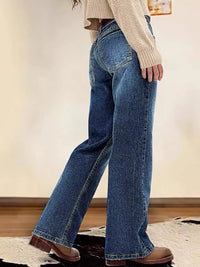 Person wearing blue jeans and a beige sweater in a minimal indoor setting