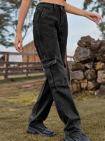 Person wearing black cargo pants in an outdoor setting with a wooden fence and rocks.