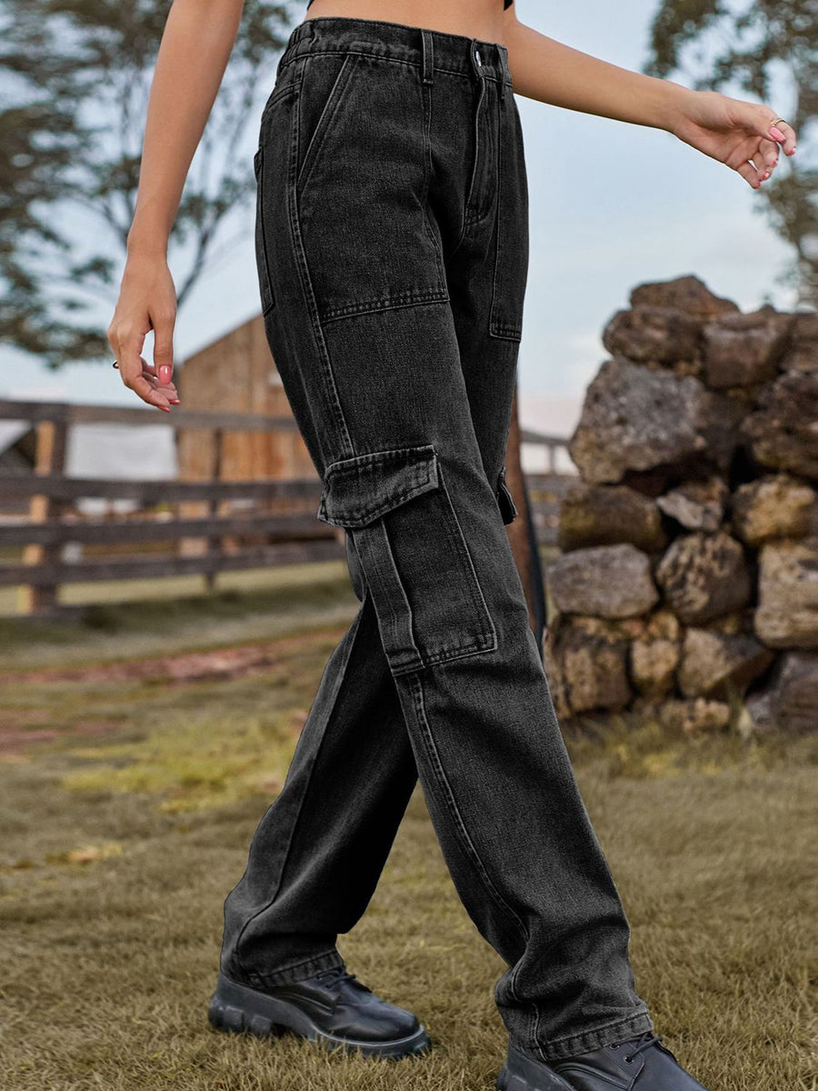 Person wearing black cargo pants in an outdoor setting with a wooden fence and rocks.