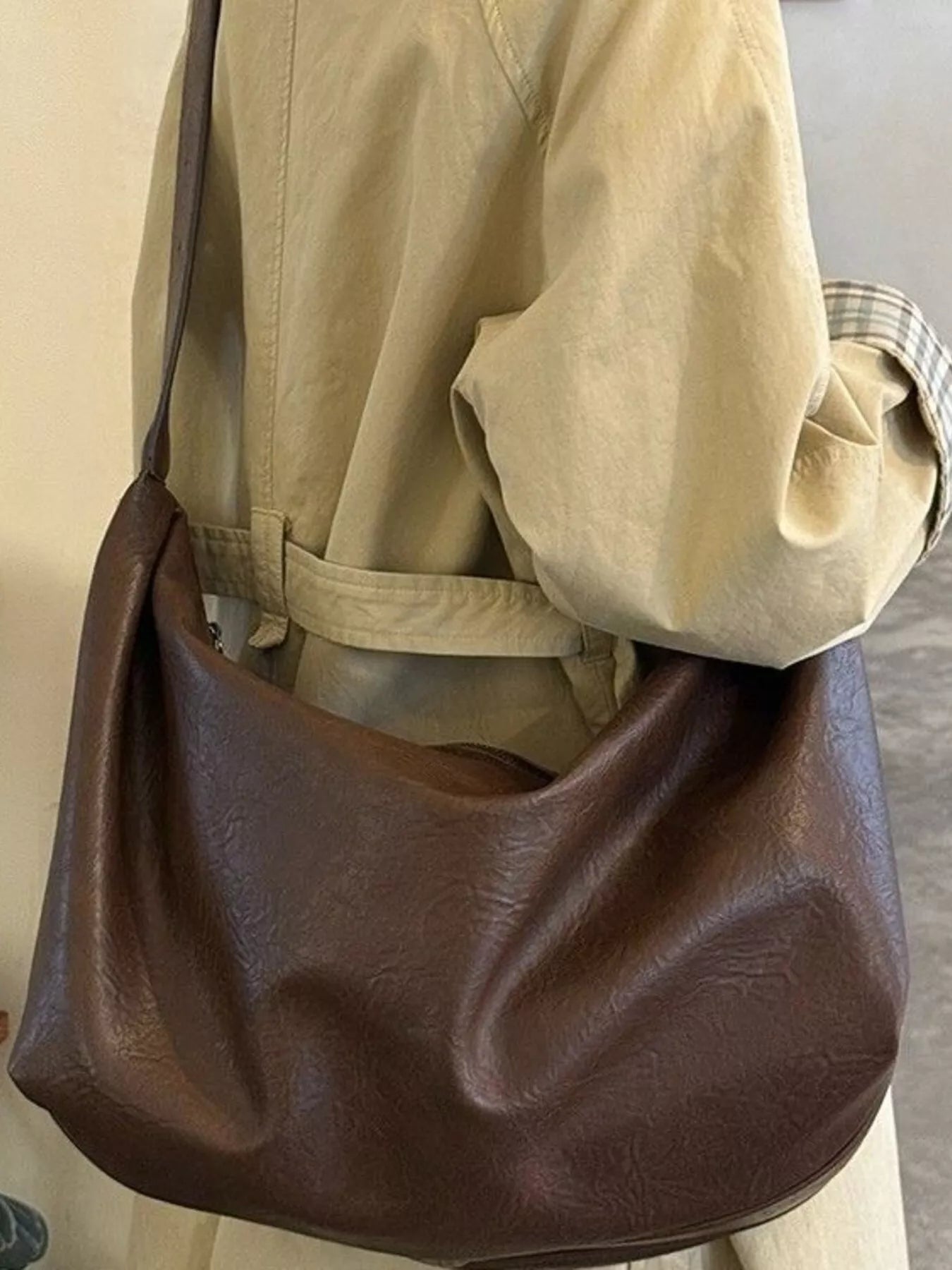 Brown leather bag held by a person wearing a beige jacket.