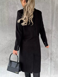 Person wearing a black coat holding a black handbag against a gray background