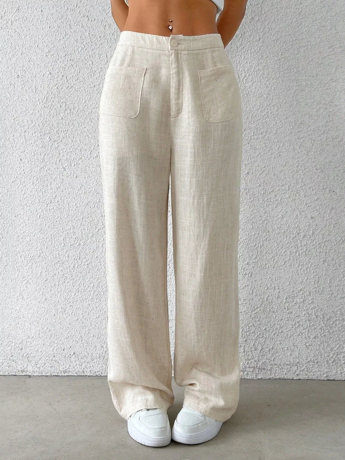 Beige linen pants worn by a person against a white wall.
