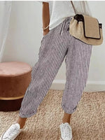 Person wearing striped pants and white sneakers with a beige bag, standing on a carpeted floor.