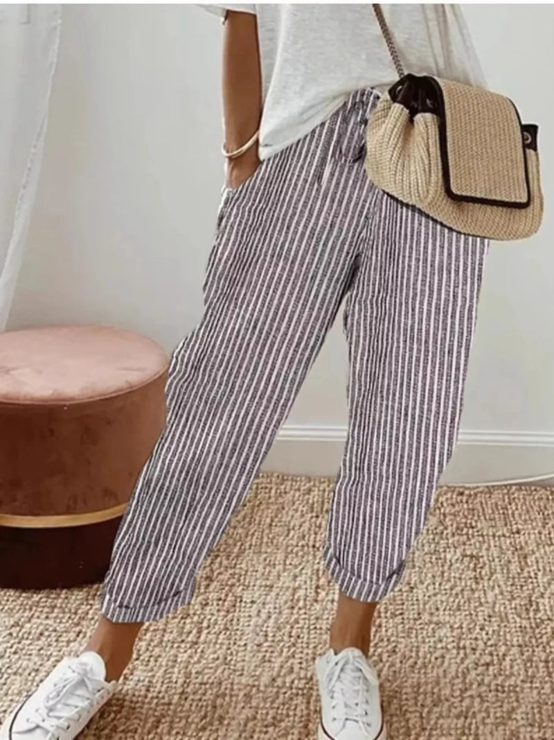 Person wearing striped pants and white sneakers with a beige bag, standing on a carpeted floor.