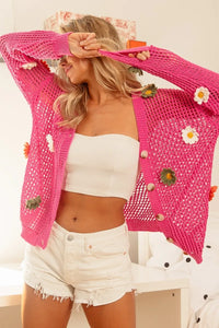 Woman wearing a pink crochet cardigan with floral decorations indoors.