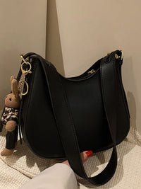 Black handbag with a keychain featuring a small rabbit figure on a neutral background