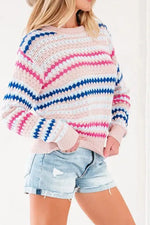A woman wearing a chunky knit crewneck sweater with horizontal wavy stripes in pink, blue, and white, paired with light-wash denim shorts.