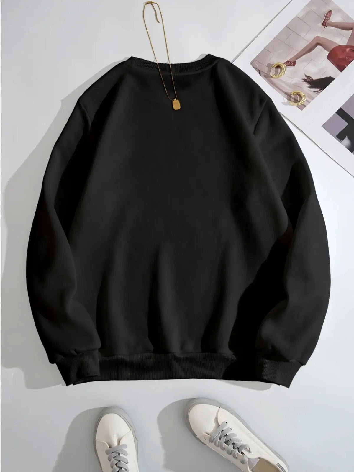 Black sweatshirt on a white background with a necklace and sneakers.