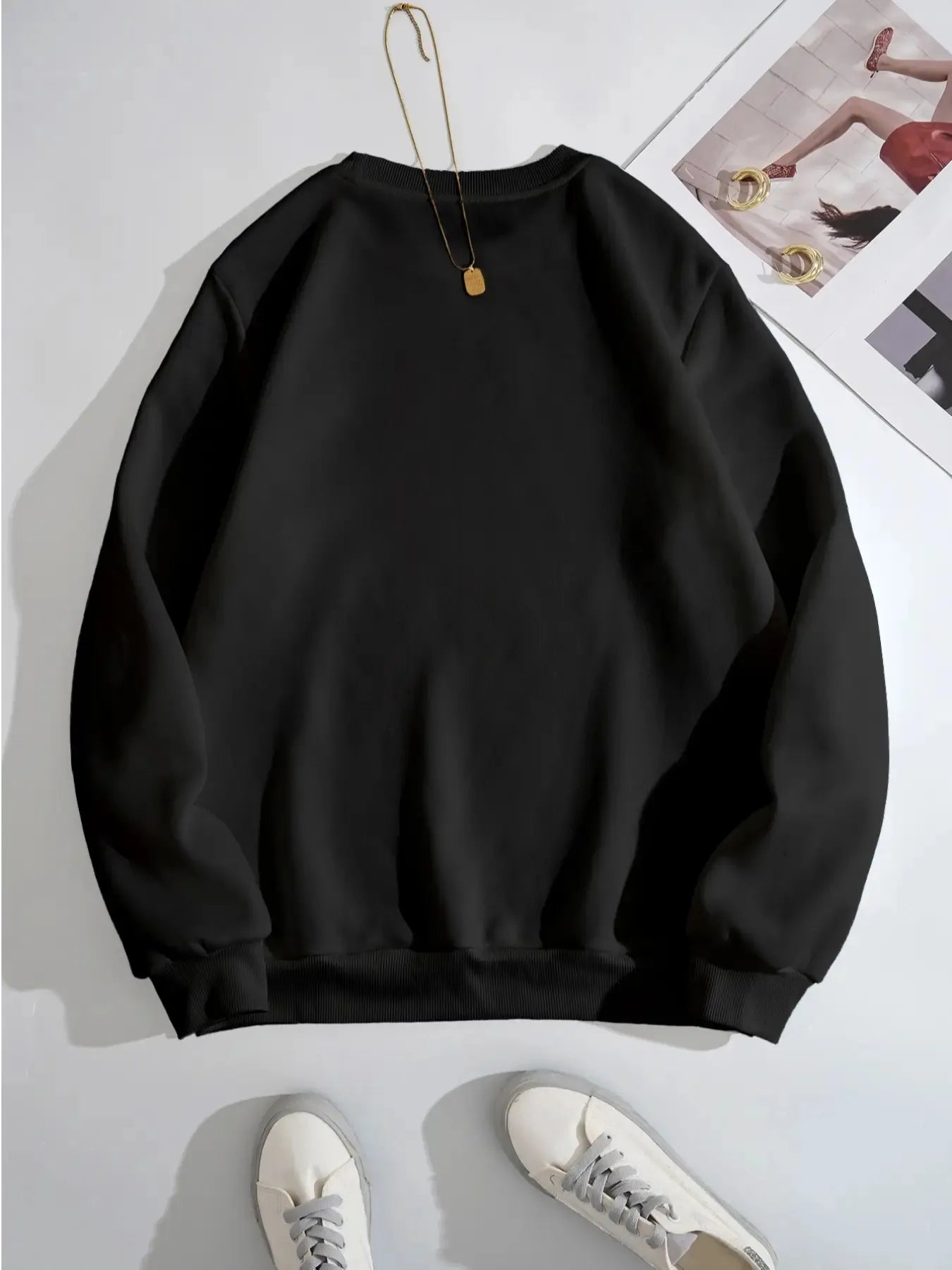 Black sweatshirt on a white background with a necklace and sneakers.