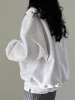 A person wearing an oversized light gray sweatshirt, shown from the back against a plain light gray background.