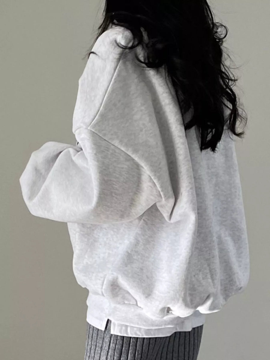 A person wearing an oversized light gray sweatshirt, shown from the back against a plain light gray background.