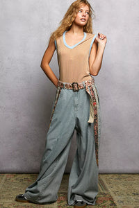 Woman wearing a beige sleeveless top and wide-leg jeans with a patterned belt against a gray background.