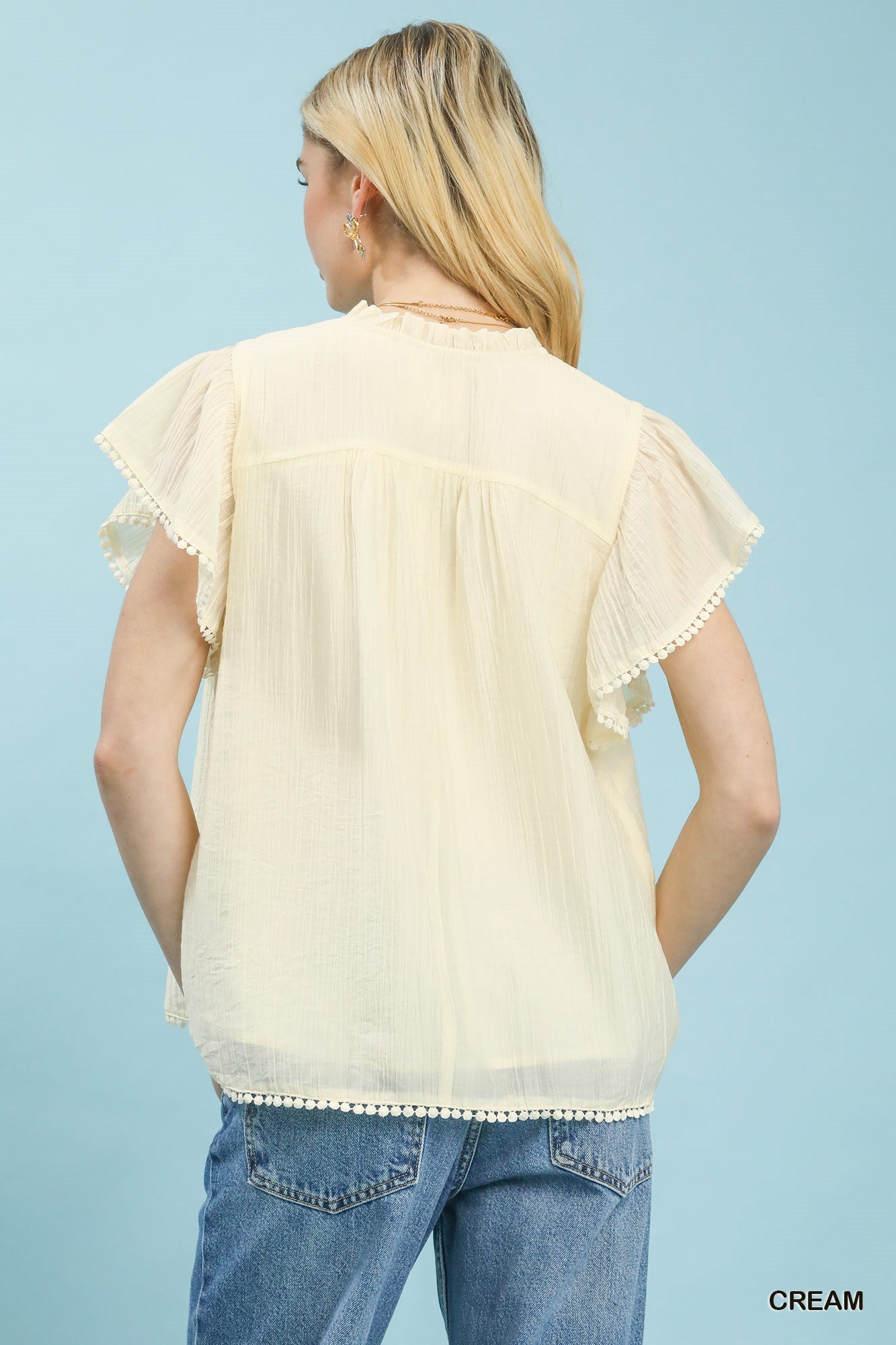 Woman wearing a cream blouse with ruffled sleeves against a light blue background