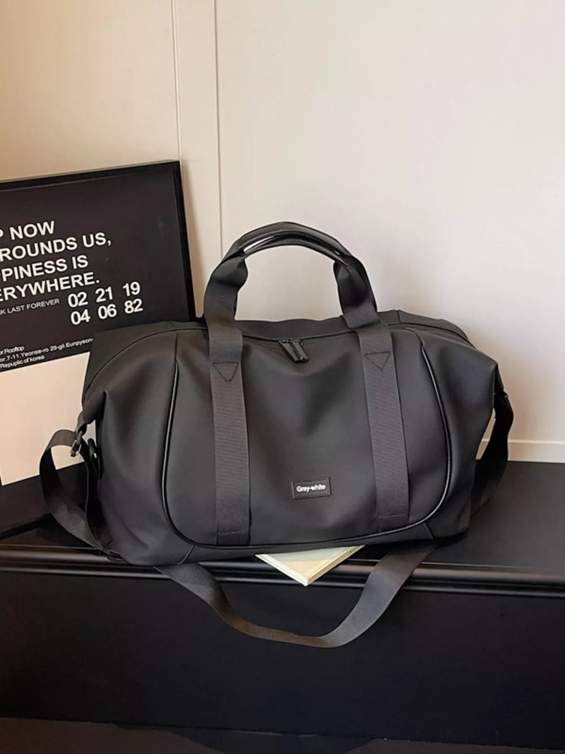 Black duffel bag on a black surface with a white wall in the background