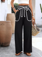 Person wearing black wide-leg pants with white trim, standing outdoors.