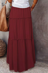 Person wearing a long burgundy skirt with a plain background