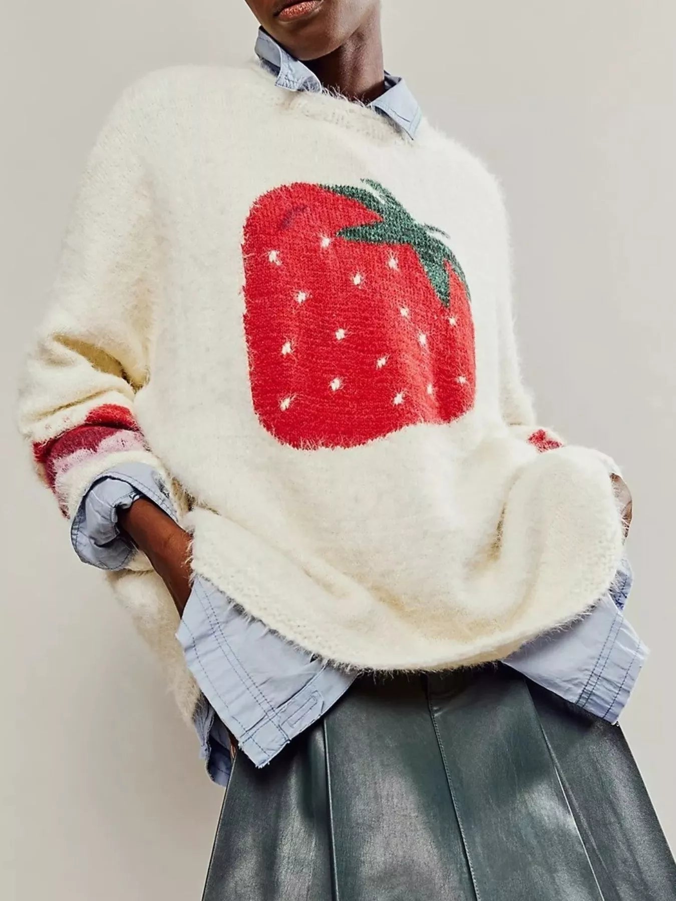 Person wearing a cream sweater with a red strawberry design on a plain background