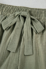 Green pleated skirt with a tie waist on a light gray background