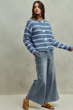 Woman wearing a blue striped sweater and jeans against a plain background