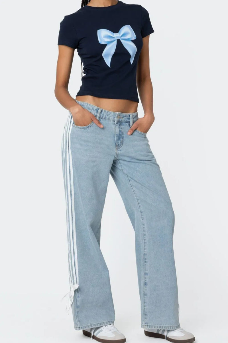 Person wearing a black t-shirt with a blue bow design and light blue jeans on a white background
