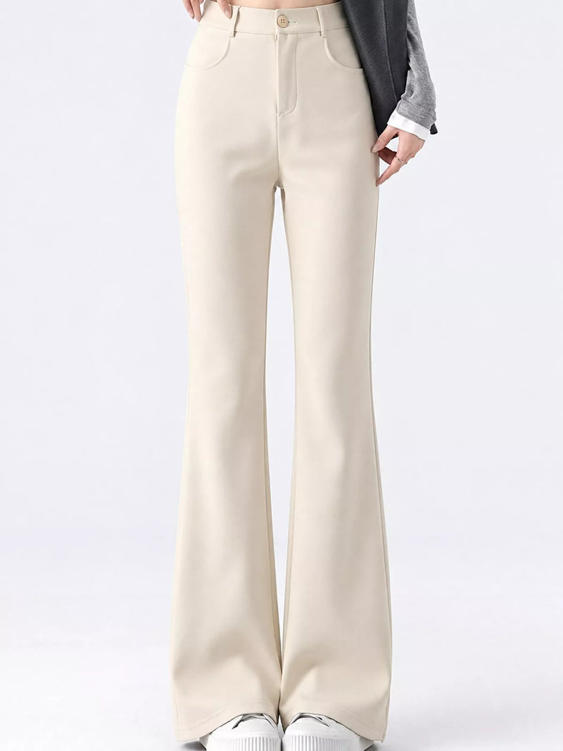 A model is wearing a pair of high-waisted, light beige flare pants with a gray blazer and white sneakers, shown from the waist down against a plain white studio background.