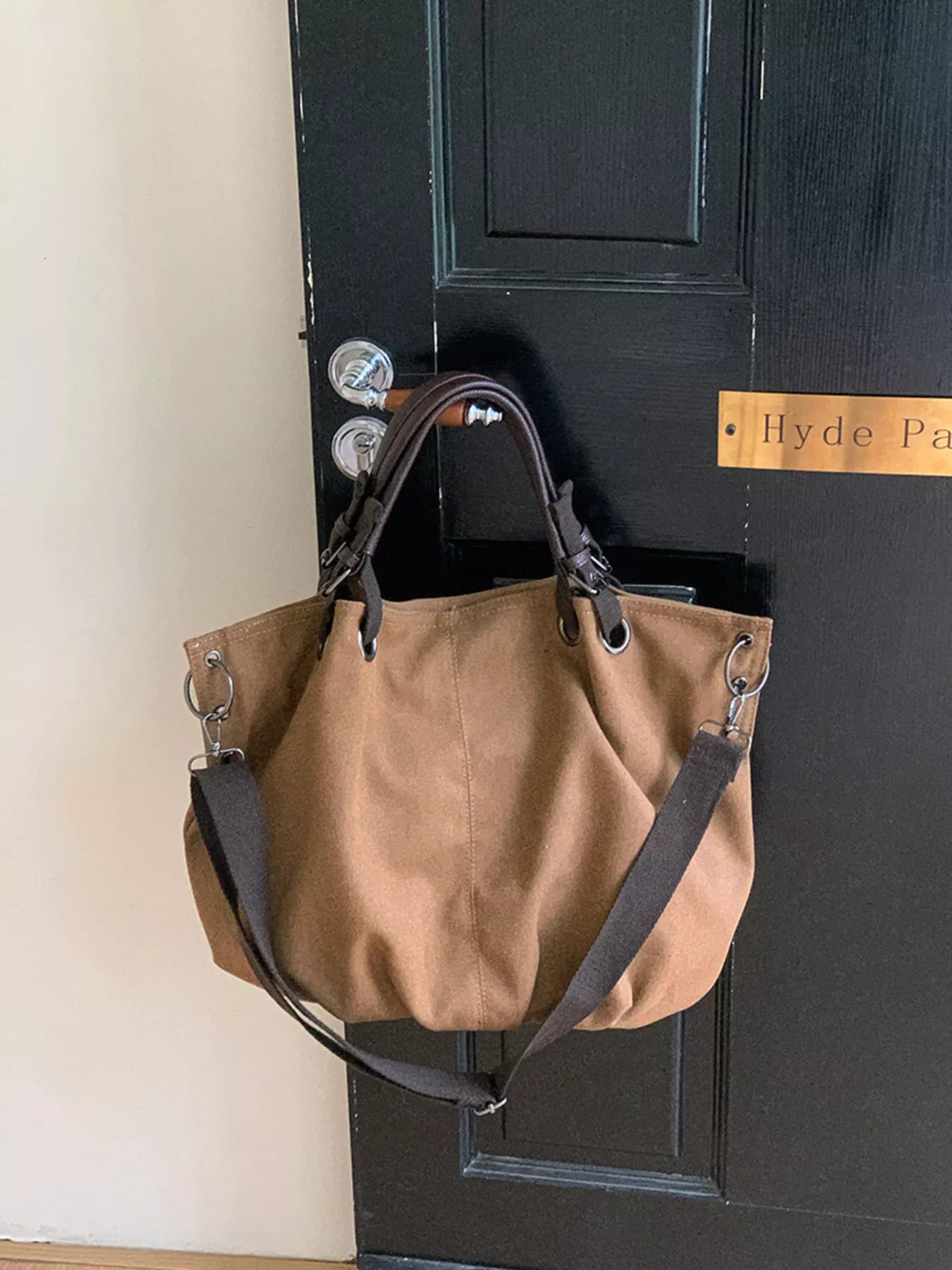 Brown handbag hanging on a doorknob of a black door with 'Hyde Park' sign.