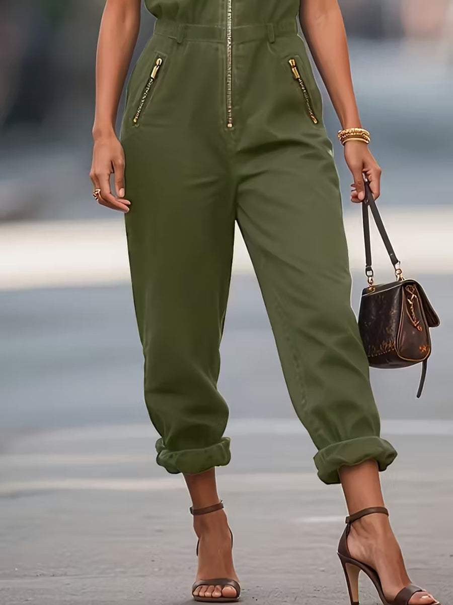Person wearing a green jumpsuit with zippers, holding a brown handbag on a blurred street background.