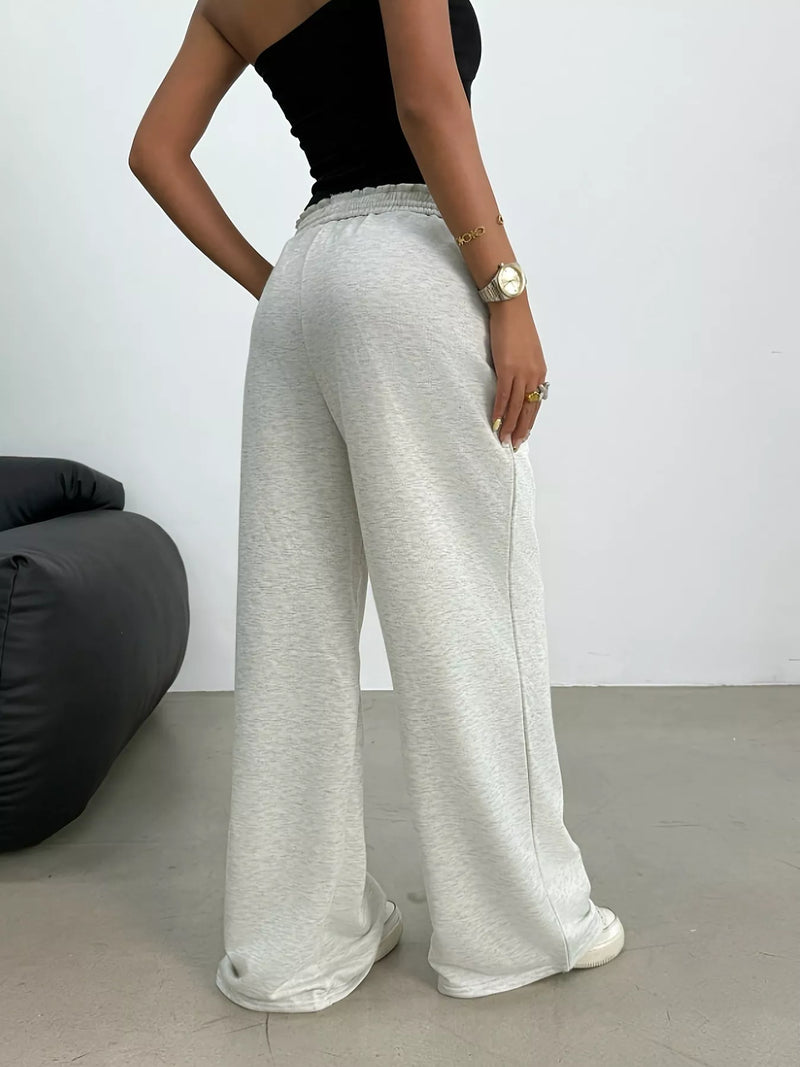 Person wearing gray wide-leg pants and a black top against a white wall.