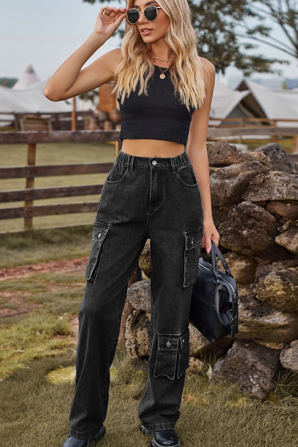 Woman in black crop top and cargo pants standing outdoors near a stone wall.