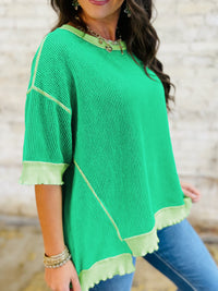 Woman wearing a green poncho with light green trim against a blurred background