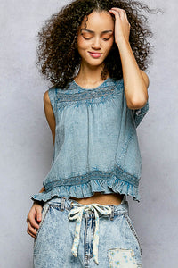 Woman wearing a blue sleeveless top and denim shorts against a gray background