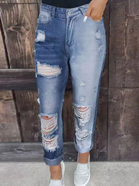 Ripped blue jeans worn by a person against a wooden background