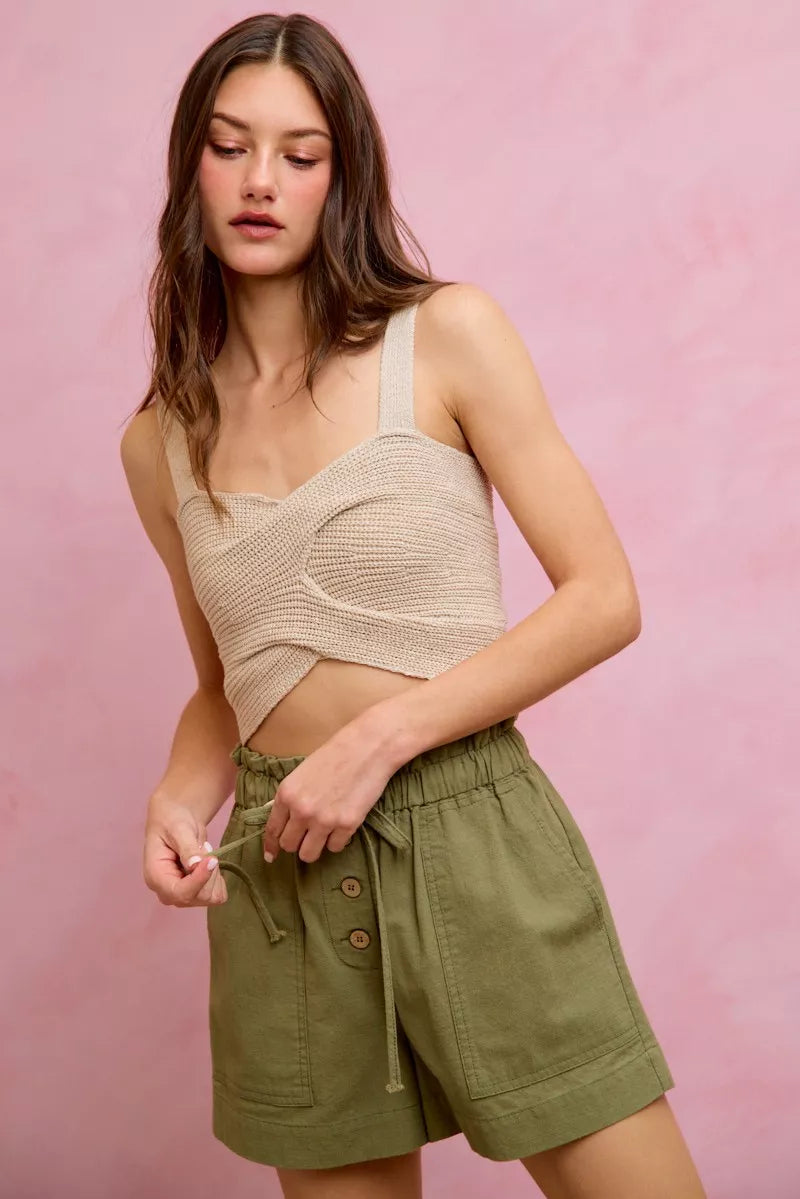 Woman wearing a beige knitted top and green shorts against a pink background