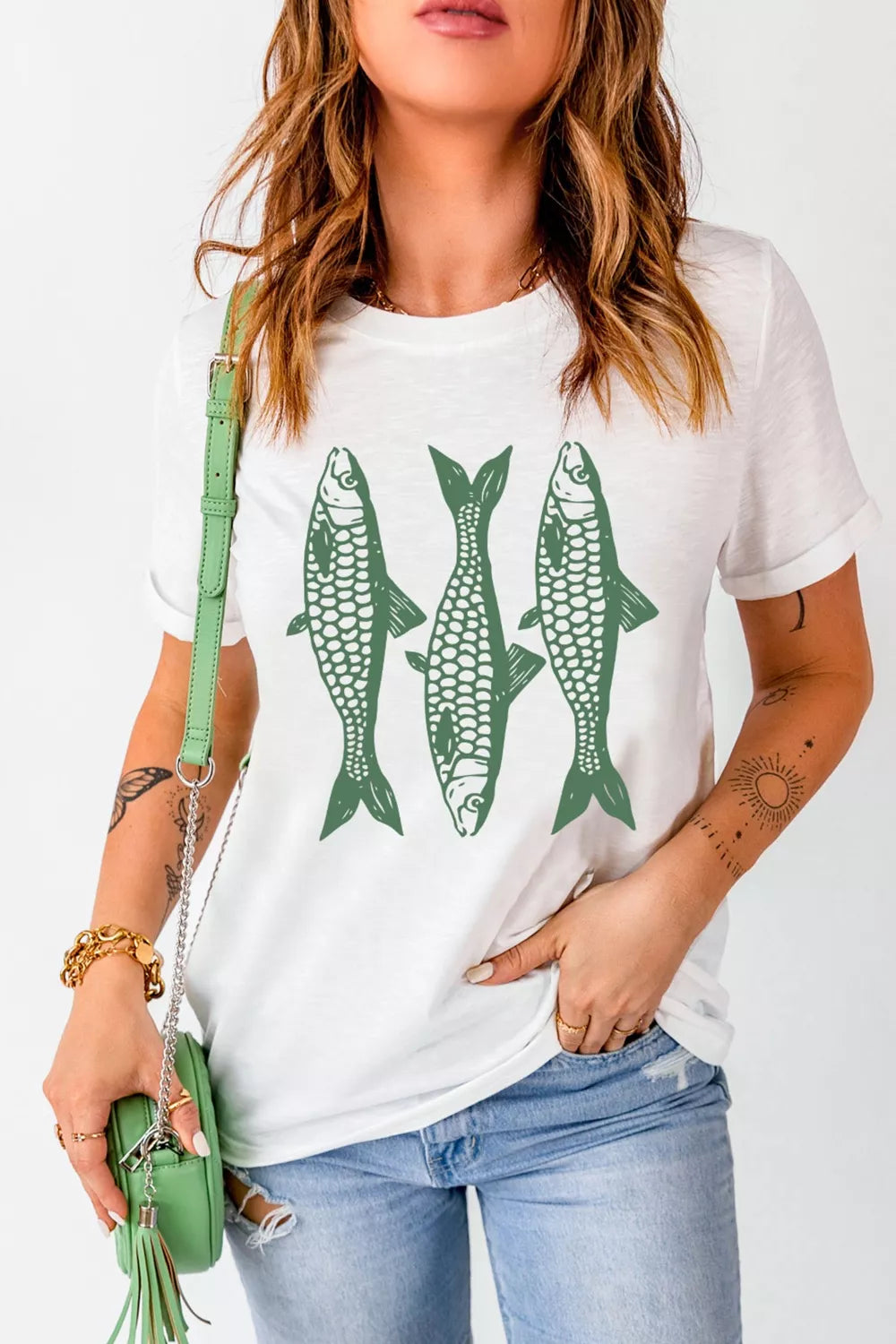 Woman wearing a white t-shirt with green fish graphics, holding a green purse.