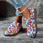 Colorful slip-on shoes with a pattern worn by a person on a gray surface.