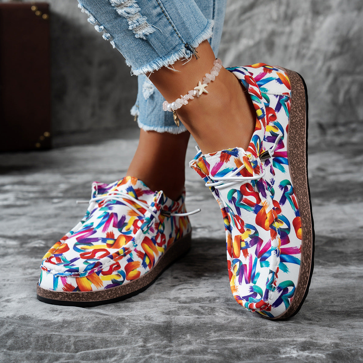 Colorful slip-on shoes with a pattern worn by a person on a gray surface.