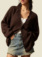 A woman wearing a dark brown fuzzy knit cardigan with a V-neck and button-front closure, styled over a white top and a denim mini skirt against a plain beige background.