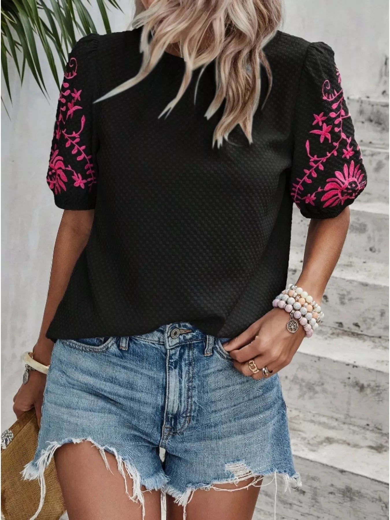 Person wearing a black top with pink floral embroidery and denim shorts.