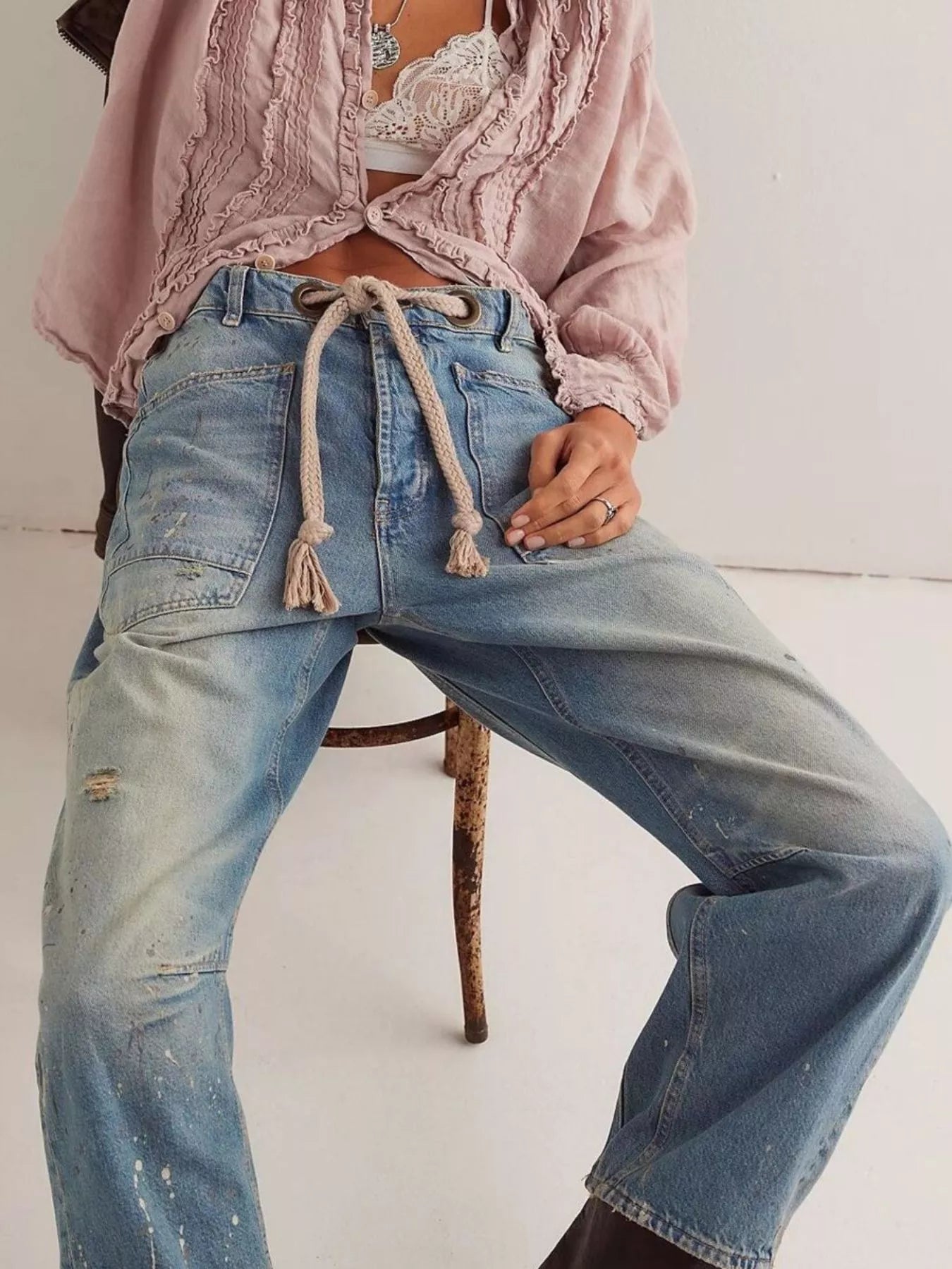 Person wearing a pink textured top and blue jeans sitting on a chair.