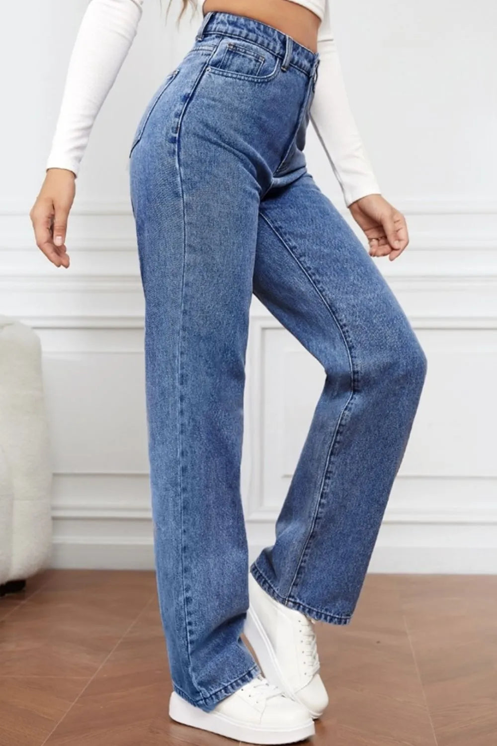 Person wearing blue jeans and white sneakers on a neutral background