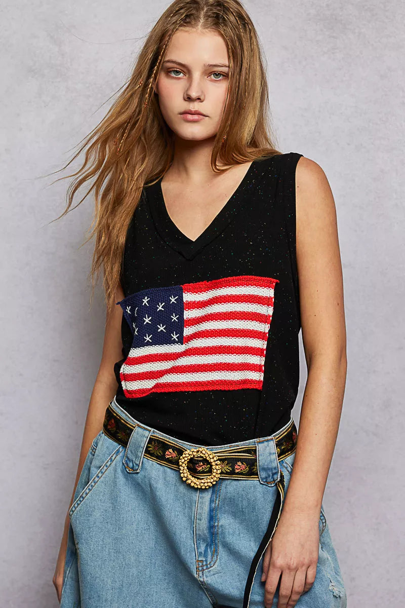 Woman wearing a black sleeveless top with an American flag design and blue jeans against a gray background