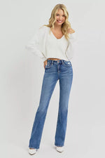 Woman wearing a white sweater and blue jeans on a plain background